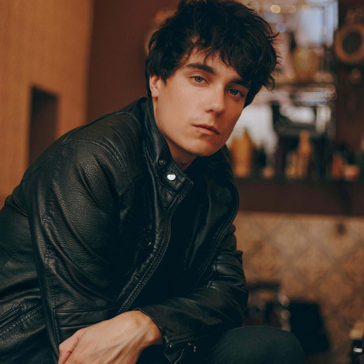 Stylish young man in a black leather jacket posing confidently indoors.