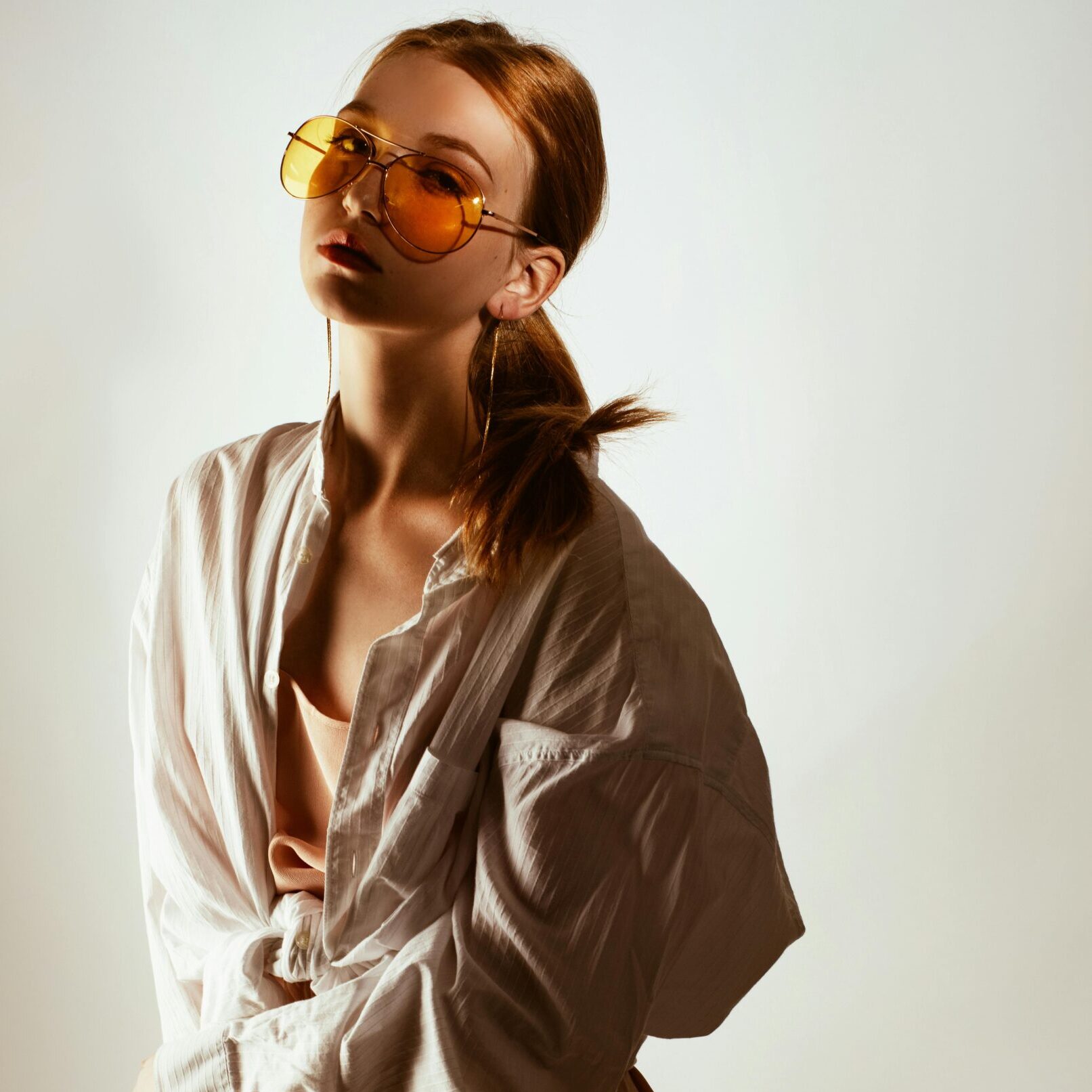 Trendy woman posing in oversized shirt and sunglasses, exuding modern fashion style.